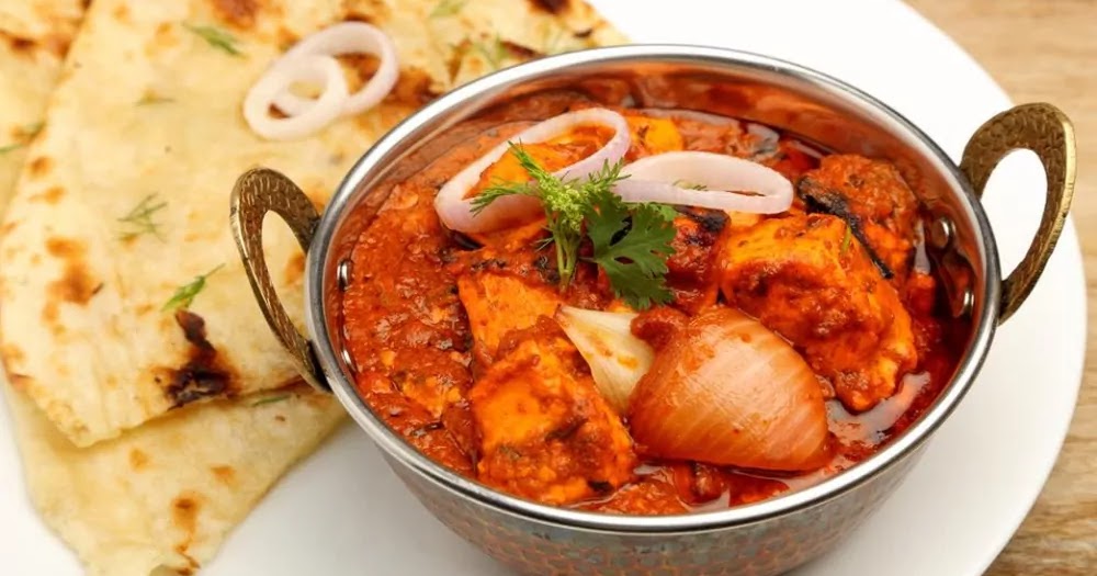 Panner Do Pyaza served in a pan with tandoori Naan and pieces of onion as a garnish.